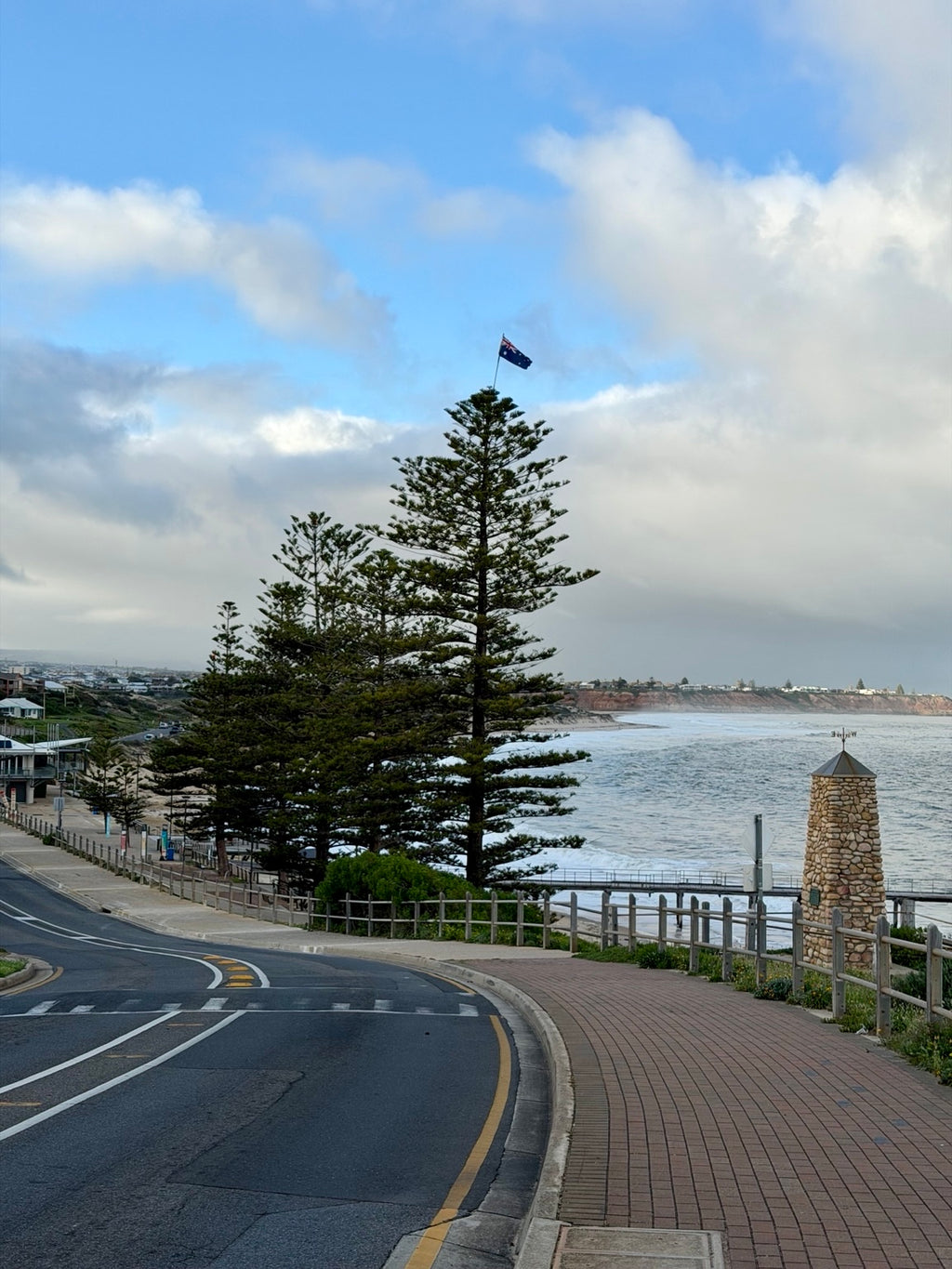 Port Noarlunga coastal road with Norfolk pine, Australian flag, stone monument and ocean